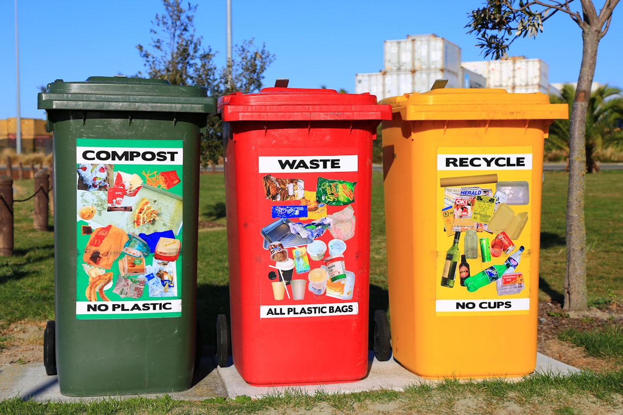Colourful wheelie bins for compost, waste, and recycling lined up on a residential street